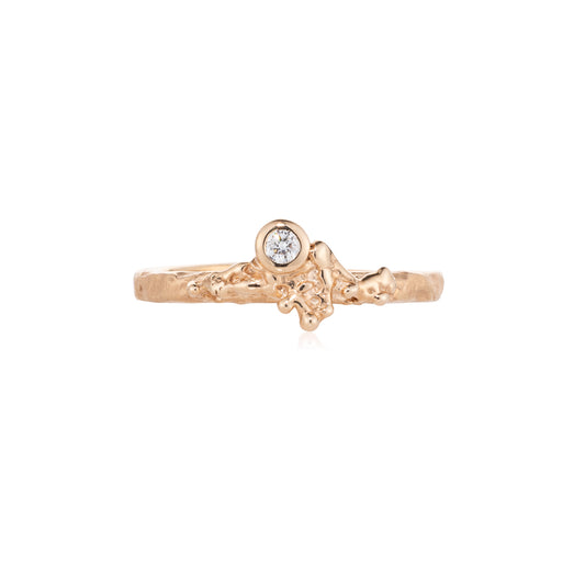 A delicate rose gold ring featuring a small round diaond in a bezel setting, with an organic, textured branch-like design on the band, shown against a plain white background.