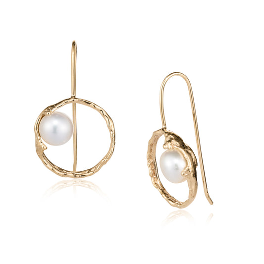 A pair of gold dangle earrings with a textured open circular frame and a white freshwater pearl, shown on a clean white background with a subtle reflection.