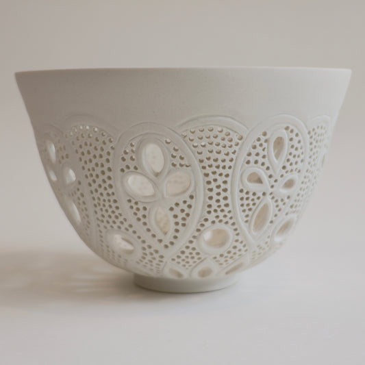 A white ceramic bowl featuring intricate laser-cut openwork patterns on the exterior, set against a plain light gray background.