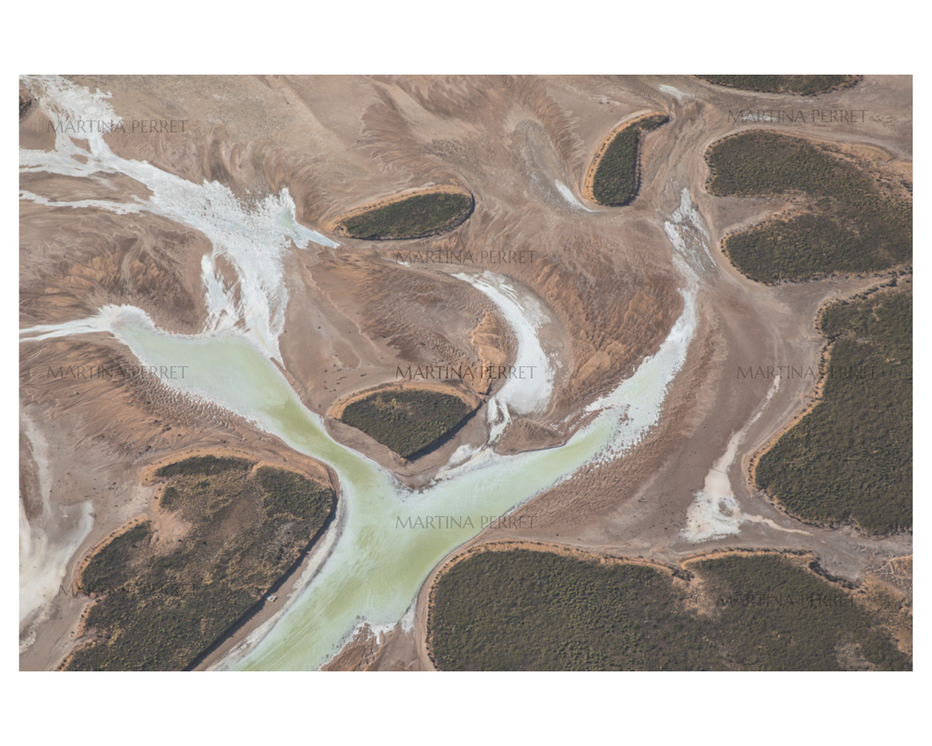 An aerial landscape photograph of a winding pale green river or inlet cutting through brown and tan terrain with dark green forested islands. Faint repeated watermark text is visible across the image.